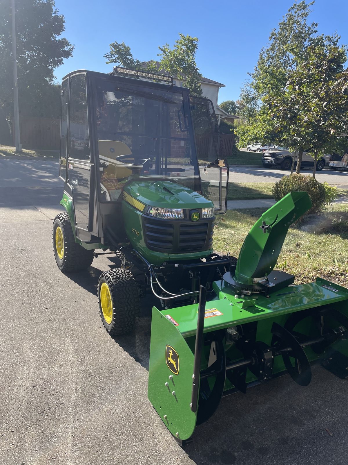 The cab tractor with its snowblower attachment on a residential street under a blue sky