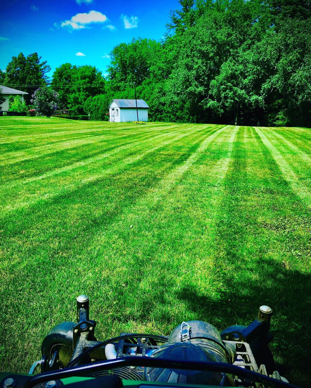 The view from the mower seat over a freshly striped lawn on a bright summer day
